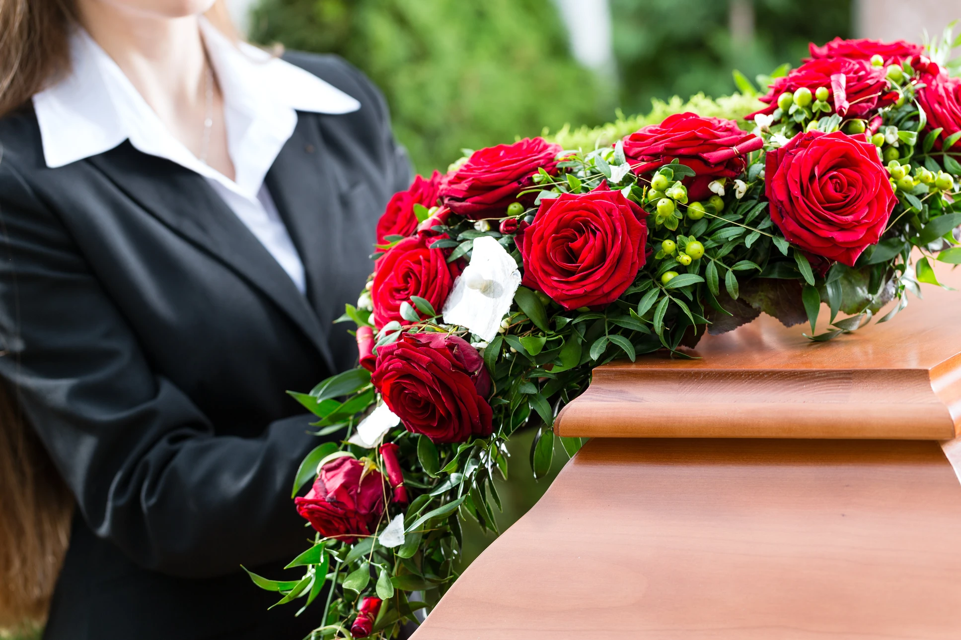 Scène de funérailles en extérieur avec femme en costume noir tenant bouquet de roses rouges près d'un cercueil en bois